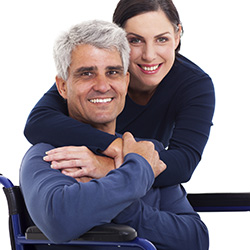 Man sitting in a wheelchair and a woman with her arms around him