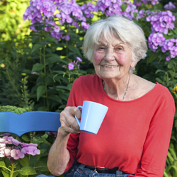 Smiling senior woman sitting on garden bench holding a mug