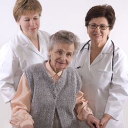 Two health care workers standing and supporting an older woman with a walking frame