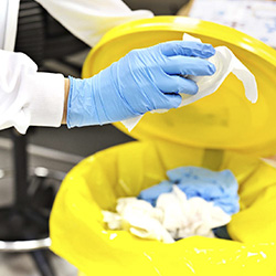 Gloved hands disposing of medical waste in a bin