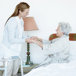 Female carer assisting elderly woman stand up from bed