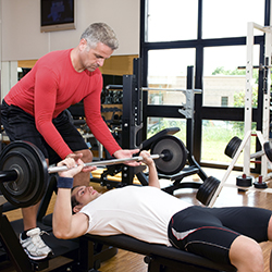 Man helping another man bench press in gym