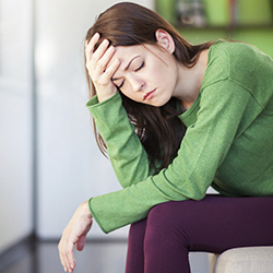 Woman with eyes closed sitting down with hand on head