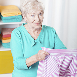 Mature woman holding a shirt with folded towels on shelves behind