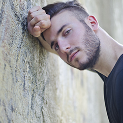 Serious man leaning on head on hand against tree