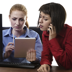 A woman using an electronic tablet while another woman talks on the phone