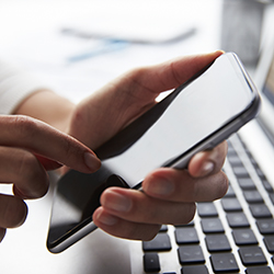 Hands holding a mobile phone at a laptop